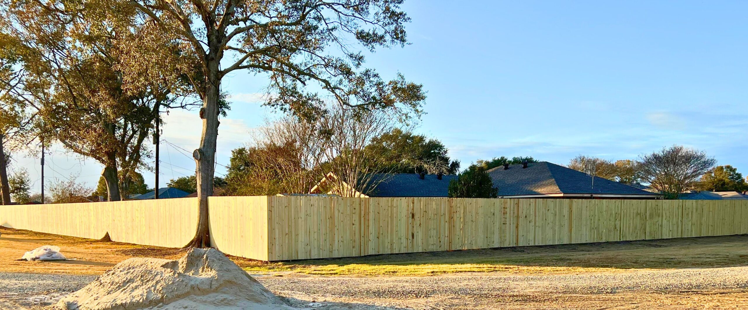 A newly built wooden privacy fence running across a backyard with mature trees, by Deane Construction