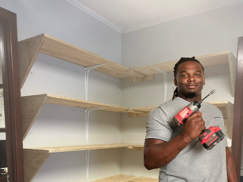 A Deane Construction carpenter with a power drill beside custom-built closet shelving he installed